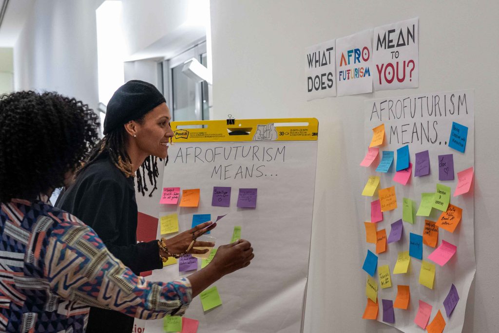 Attendees placing sticky notes on an interactive question on a wall answering "What does Afrofuturism Mean to you?"