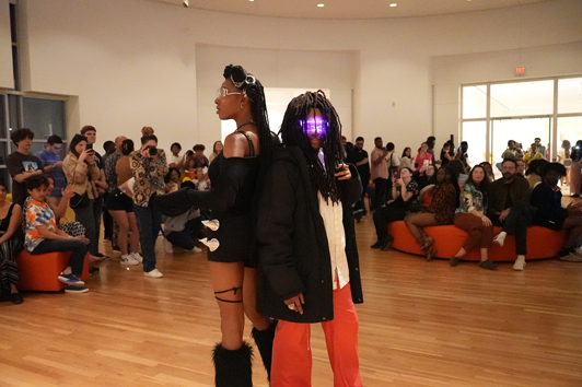Two models pose in front of crowd while wearing afrofuturist clothes