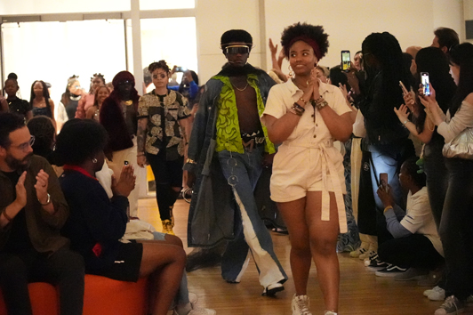 A line of Fashion Show Models walking into a crowded room of people clapping.