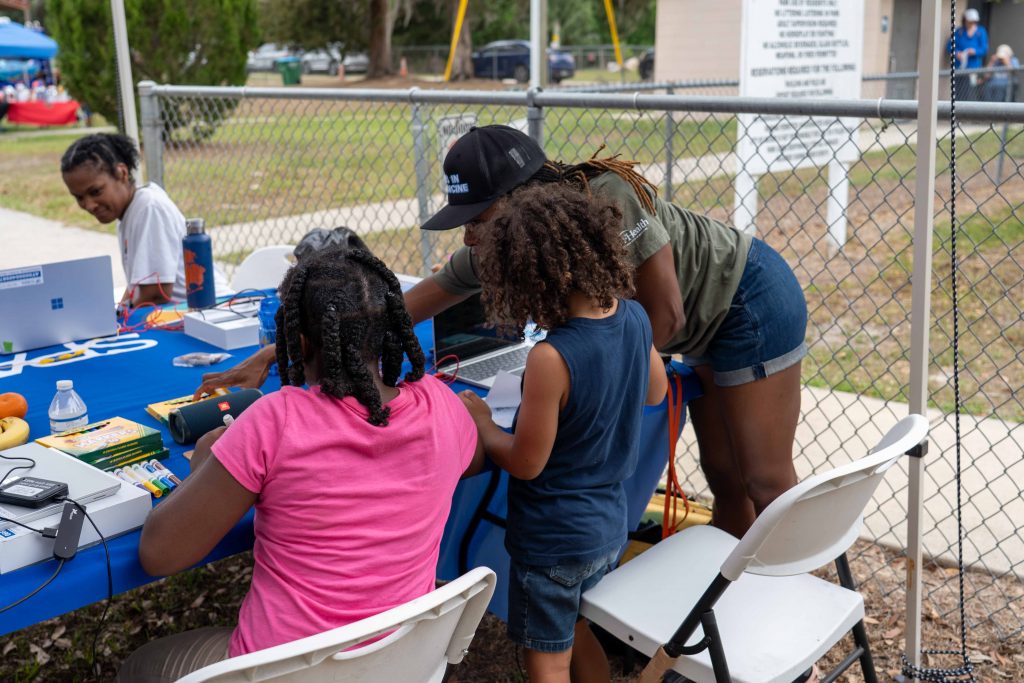 Two youth sit a table with their backs to the camera. The table has various art supplies on it.