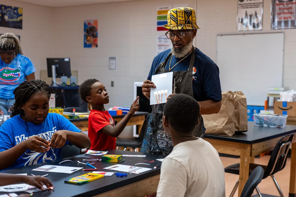 A young boy reaches to touch a piece of paper being held up by the artist facilitator.