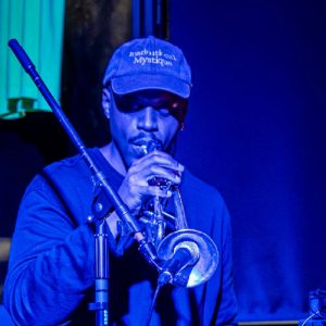 man playing a brass instrument into a mic with moody lighting