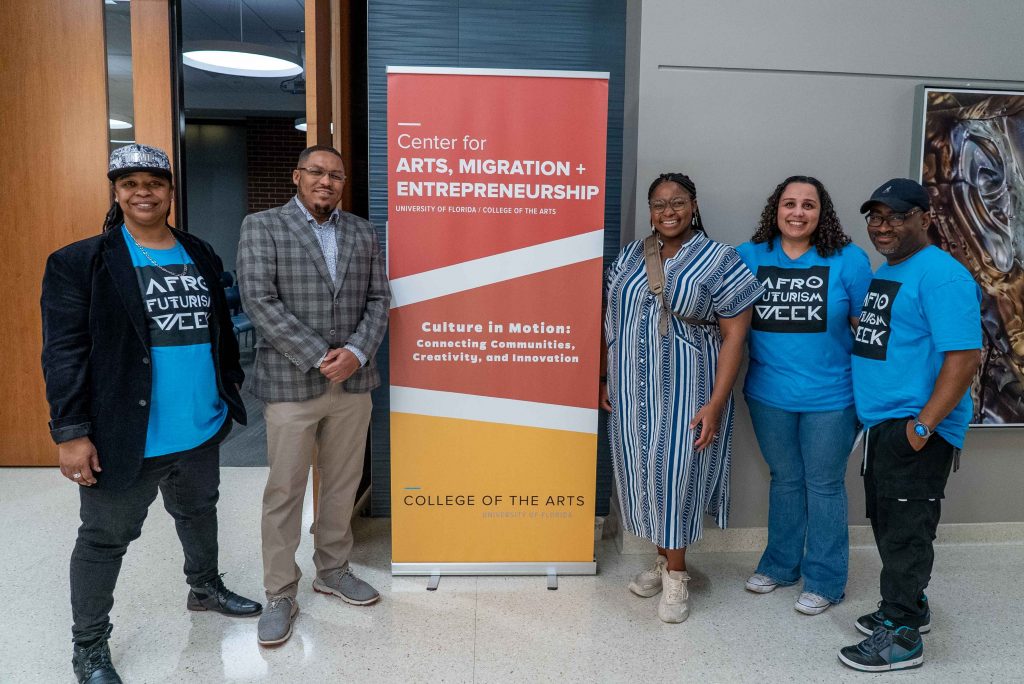 Five people standing next to a banner that reads Center for Arts, Migration + Entrepreneurship